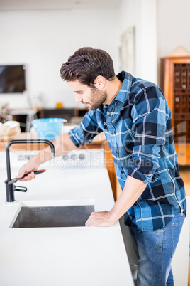 Man fixing tap with tool in the kitchen