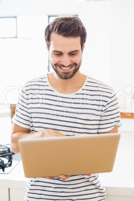 Happy man using laptop in kitchen