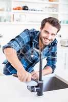 Portrait of happy man fixing tap with tool in the kitchen