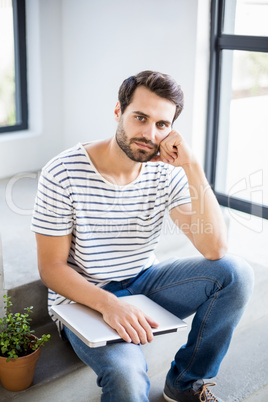Portrait of thoughtful man sitting on steps with laptop