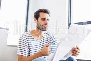 Man on steps having cup of coffee while reading newspaper
