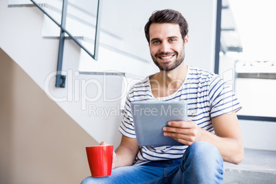 Portrait of happy man on steps holding coffee cup and digital ta