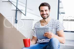 Portrait of happy man on steps holding coffee cup and digital ta