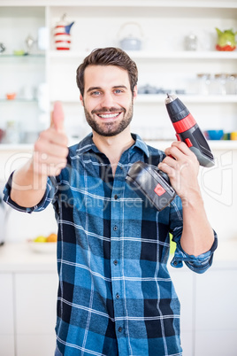 Portrait of man showing thumbs up while holding drill machine