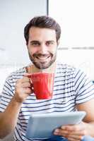 Portrait of happy man holding digital tablet while having cup of