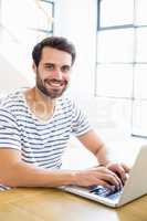 Portrait of happy man sitting on table and using laptop
