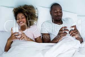 Happy couple using mobile phone on bed
