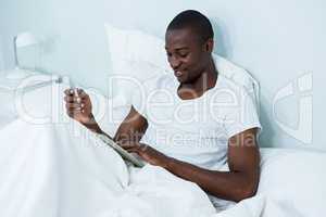 Happy young man using digital tablet and phone on bed