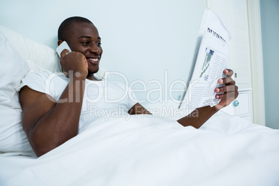 Man reading newspaper while talking on phone