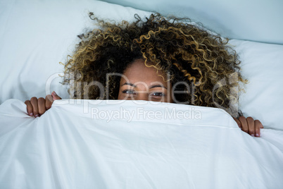 Woman hiding under blanket on bed