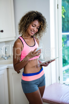 Young woman using phone and digital tablet in kitchen Young woman using phone and digital tablet in kitchen