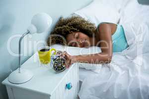 Woman stopping alarm while sleeping on bed