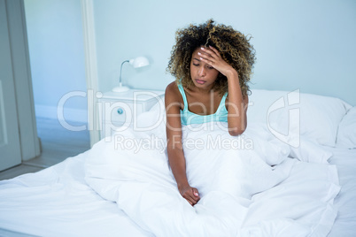 Tensed woman sitting on bed in bedroom