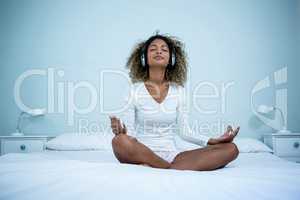 Woman listening to music on head phones while meditating on bed