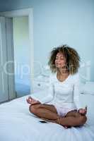 Woman listening to music on phone while meditating on bed