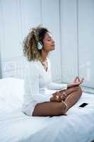 Woman listening to music on head phones while meditating on bed