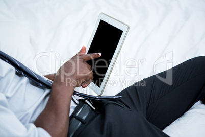 Mid-section of man using digital tablet on bed