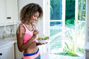 Happy woman having bowl of salad while listening to music
