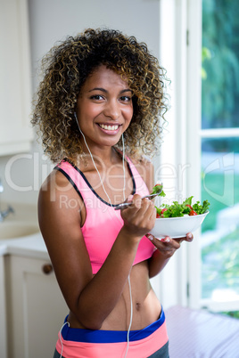 Happy woman having bowl of salad while listening to music