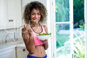 Happy woman having bowl of salad while listening to music