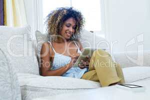 Happy woman sitting on sofa and using a digital tablet