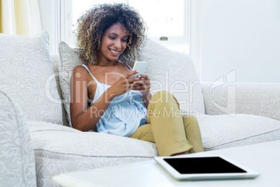 Young woman sitting on sofa and text messaging on phone