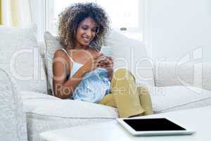 Young woman sitting on sofa and text messaging on phone