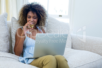Woman having wine while using laptop