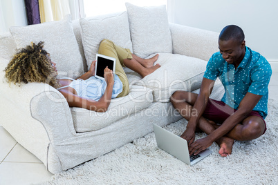 Couple using digital tablet and laptop in living room