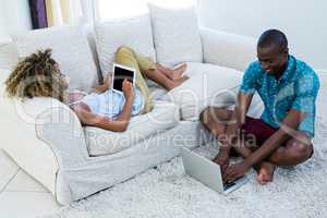 Couple using digital tablet and laptop in living room