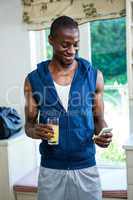 Young man holding a glass of juice while text messaging on phone