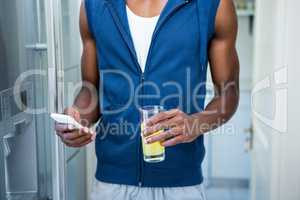 Mid- section of man holding a glass of juice while text messagin