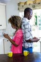 Couple standing back to back and using mobile phone