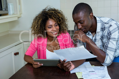 Happy couple checking bills while using digital tablet