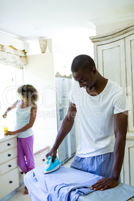 Young man ironing a shirt in kitchen