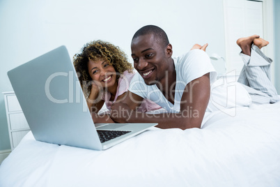 Young couple lying on bed and using laptop