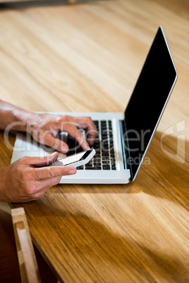 Man text messaging on phone while using a laptop