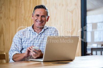 Smiling senior man using smartphone and laptop