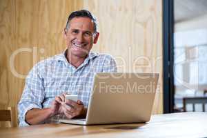 Smiling senior man using smartphone and laptop