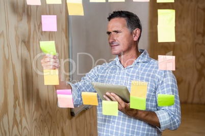 Thoughtful man holding digital tablet and sticky notes