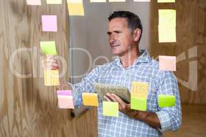 Thoughtful man holding digital tablet and sticky notes