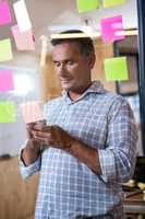 Man using mobile phone and sticky notes on window