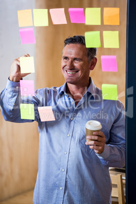 Man writing on sticky notes and holding coffee