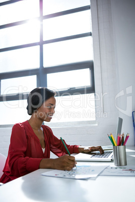 Woman writing on paper while using laptop