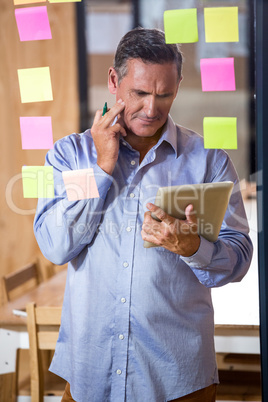 Thoughtful man looking at digital tablet and sticky notes on win