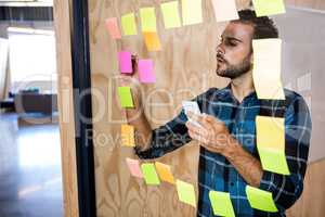 Man using mobile phone while writing on sticky notes