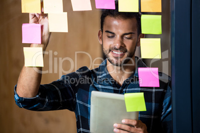 Man using digital tablet while writing on sticky notes