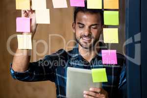 Man using digital tablet while writing on sticky notes