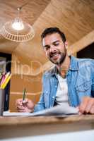 Smiling man in office writing in a notepad