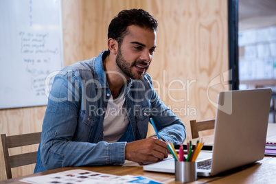 Man writing note on diary while using laptop